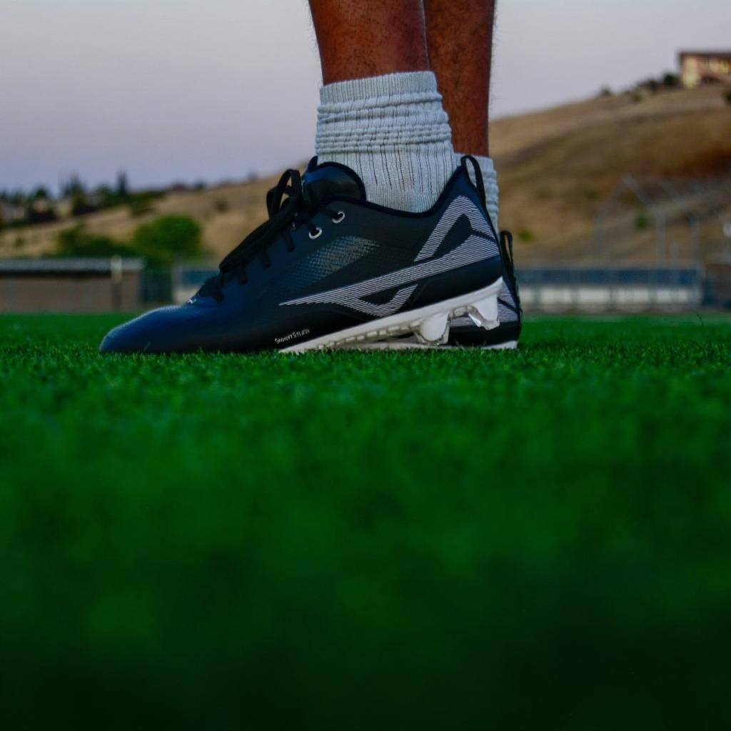 On-field shot of black/white Caddix men’s low football & lacrosse cleats that use patented Smart Studs that spin and flex to reduce ACL tears and ankle injuries