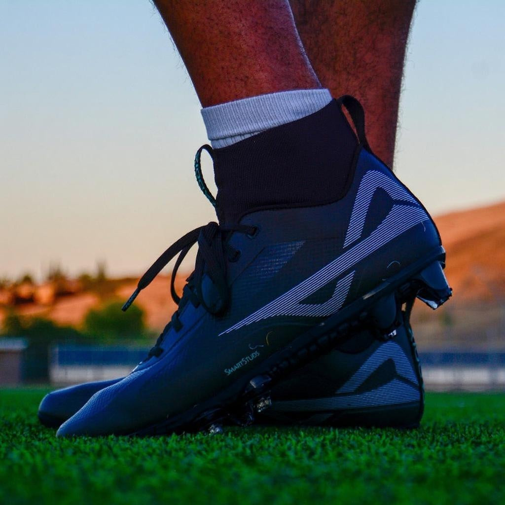 Low angle shot of Caddix men’s black/black mid football & lacrosse cleats with patented Smart Studs that flex and spin to reduce ACL tears and ankle injuries