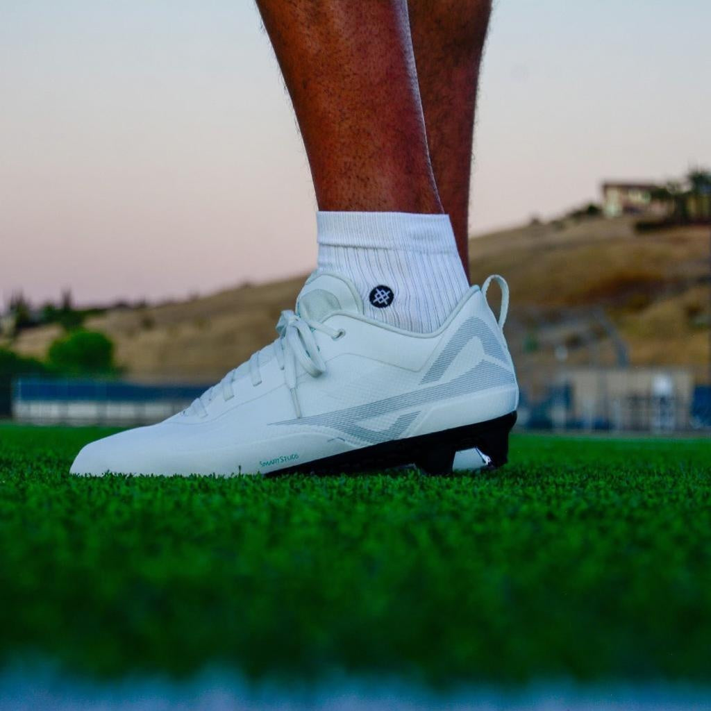 On-field view of Caddix low white/black men’s football & lacrosse cleats that use patented Smart Studs to reduce the stress that causes non-contact ACL injuries