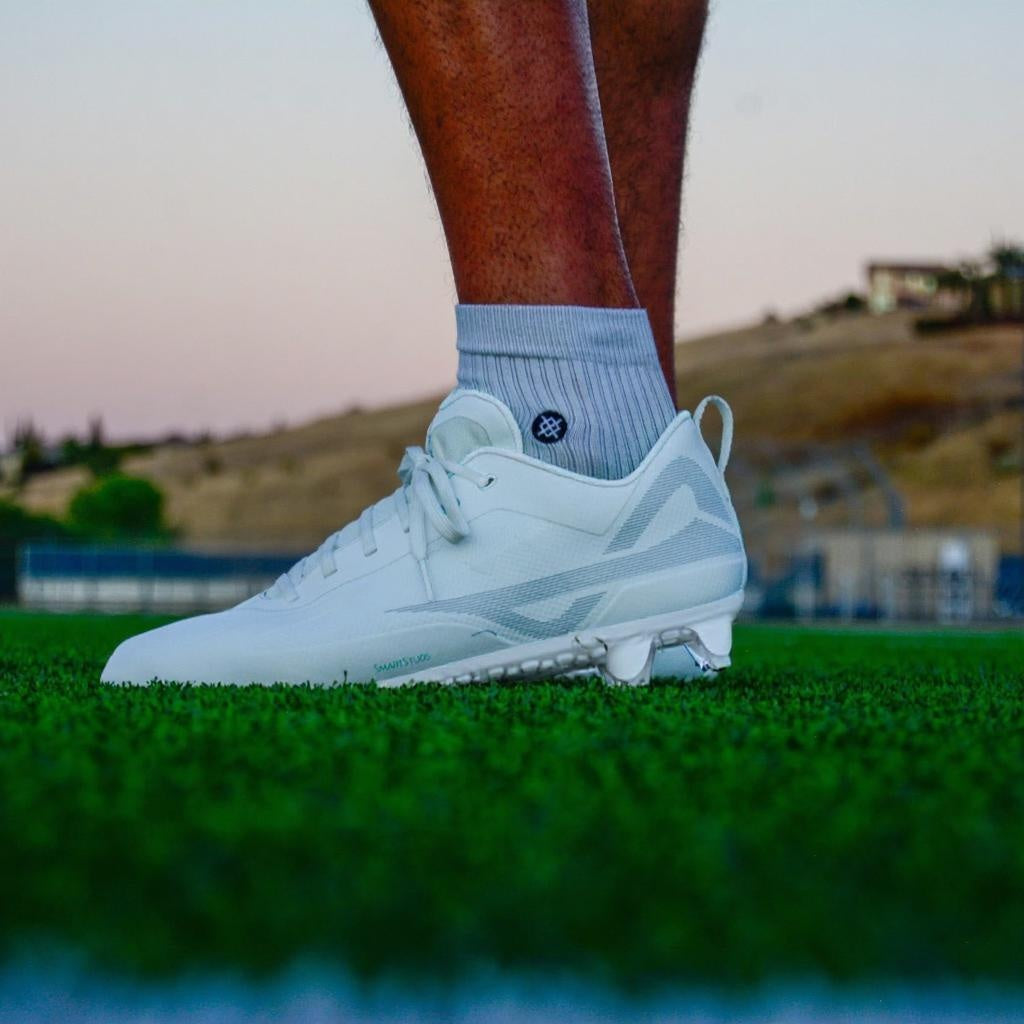 Field level view of Caddix low white/white men’s football & lacrosse cleats with patented Smart Studs that reduce non-contact ACL injuries