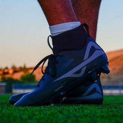 Low angle shot of Caddix men’s black/black mid football & lacrosse cleats with patented Smart Studs that flex and spin to reduce ACL tears and ankle injuries